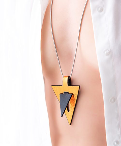 Collana con pendente in pelle di colore oro/nero , catena in acciaio. Collana indossata da modella vestita in bianco